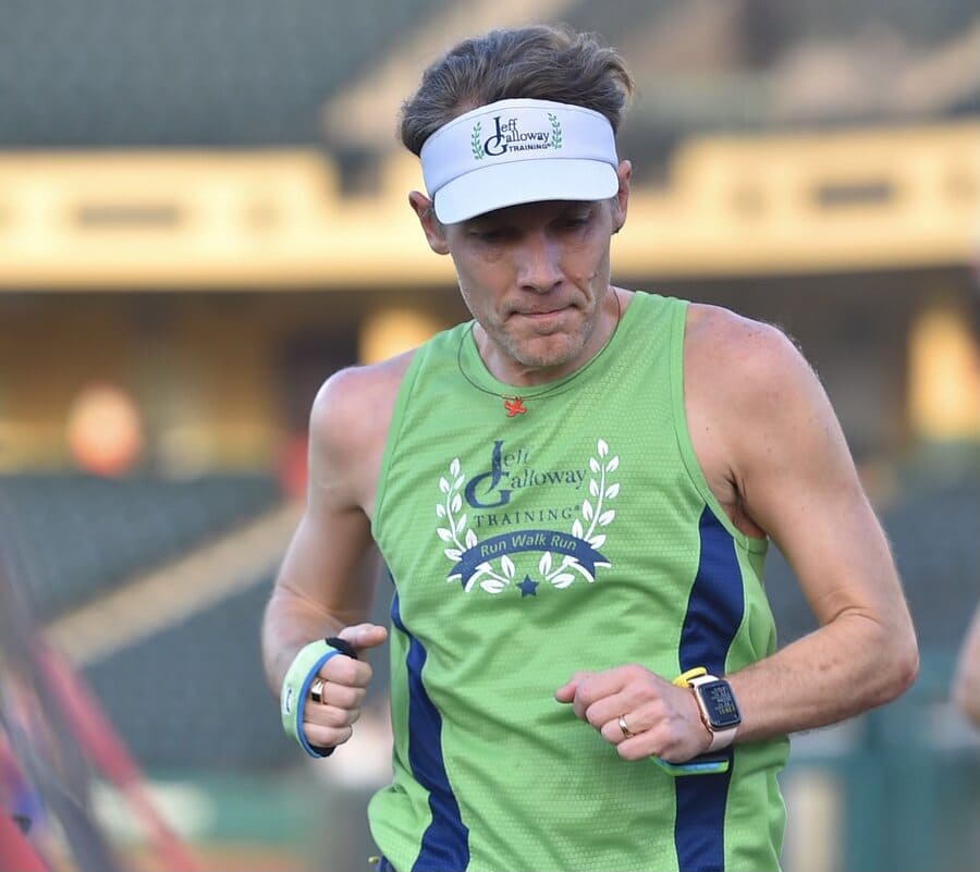 Man running race in green tank top, focused expression.