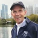 Jeff Galloway smiling near a lake with city skyline in the distance.