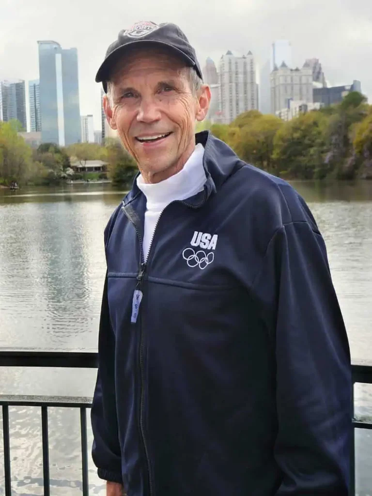 Jeff Galloway smiling near a lake with city skyline in the distance.