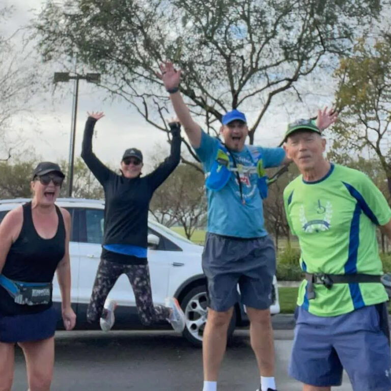Four excited runners celebrating outdoors with arms raised