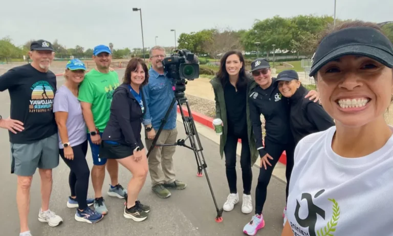 Group of runners posing with TV camera crew outdoors