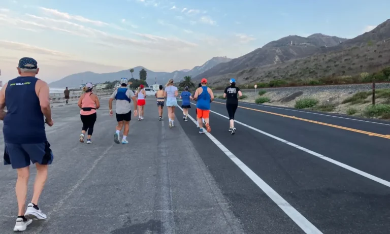Group of runners jogging along coastal road with mountains